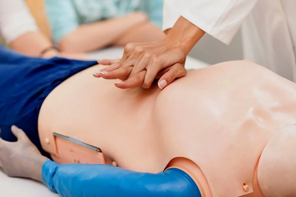 Medical professional performing chest compressions on a CPR mannequin during training.